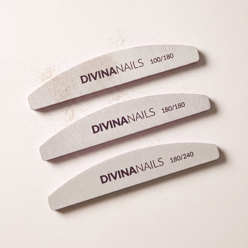 Tre lime mezzaluna Divina Nails di grana 100/180, 180/180 e 180/240 allineate dall'alto, dalla piu' grossa alla piu' fine, con la polvere di limatura