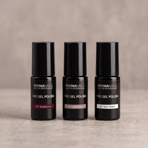 THE GEL POLISH 137 BOURGOGNE, 66 JAZZ NUDE e 01 SOFT WHITE di DIVINA NAILS allineati su un piano di cemento: i tre colori di una french manicure colorata, la lunetta bordeaux, il nude del letto ungueale e il bianco