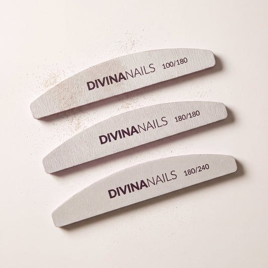 Tre lime mezzaluna Divina Nails di grana 100/180, 180/180 e 180/240 allineate dall'alto, dalla piu' grossa alla piu' fine, con la polvere di limatura